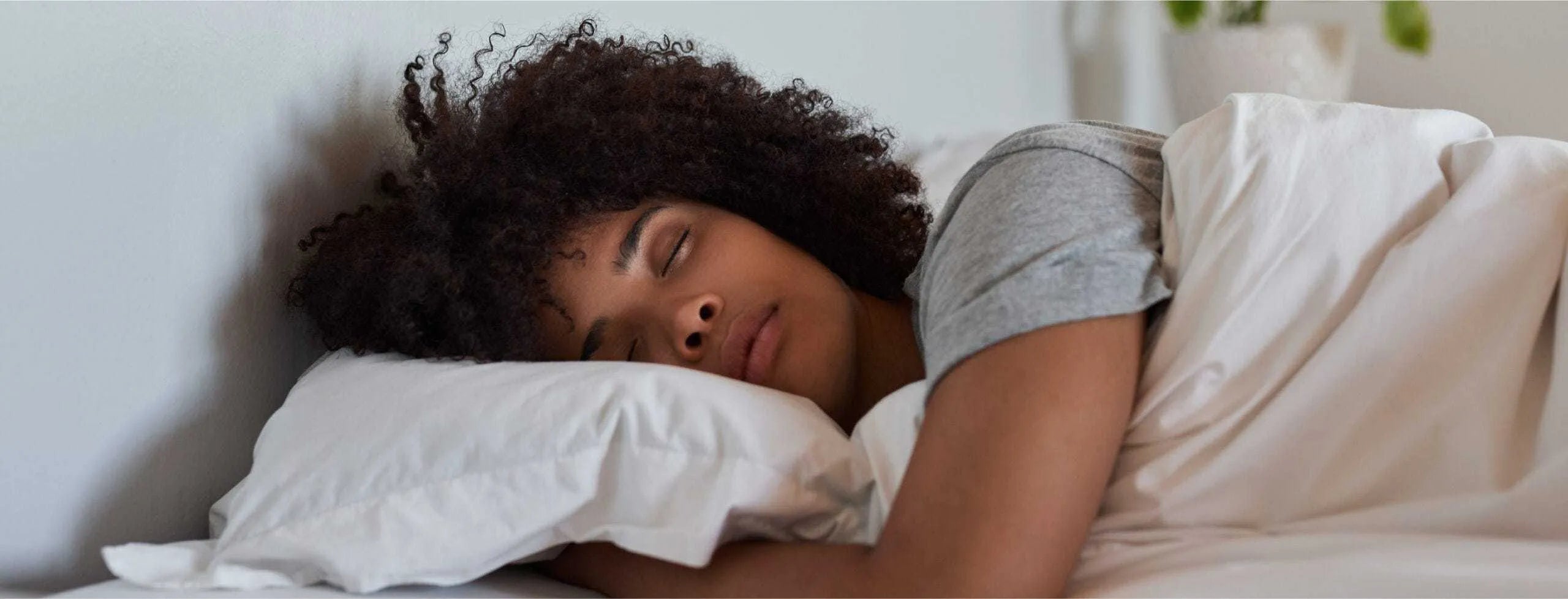 A woman asleep in a gray shirt with white sheets.