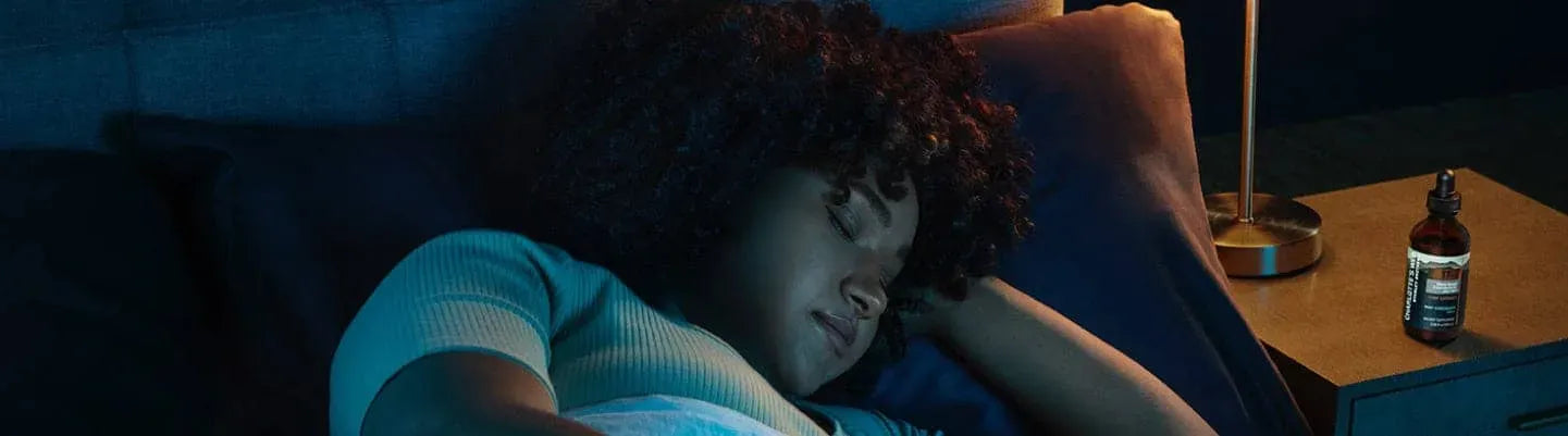 A person asleep with a bottle of Charlotte's Web CBD Oil tincture on their nightstand.