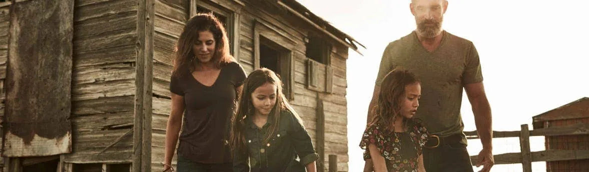 A family of four on a farm with the sun shining in the background.