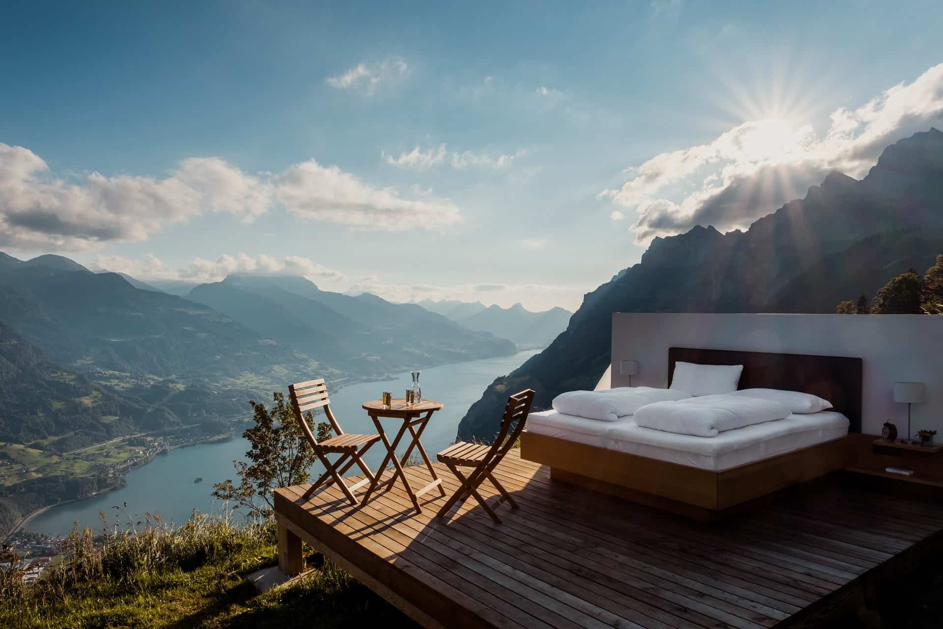A bed on a platform in the middle of nature overlooking a lake.