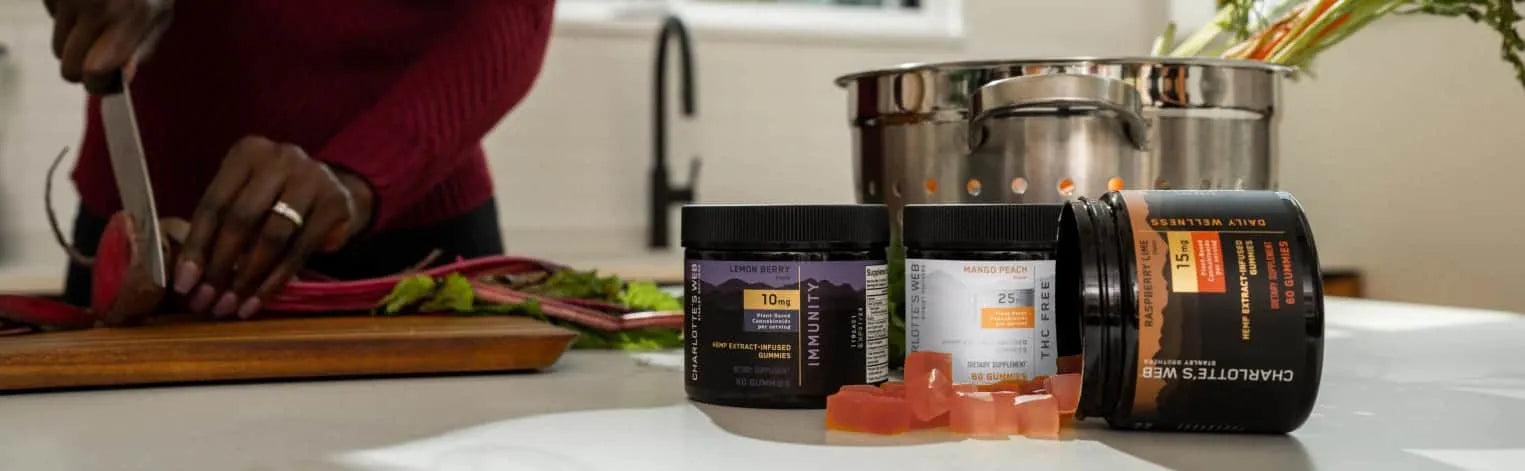 Three Charlotte Web's products on a kitchen counter with a person cutting vegetables in the background.