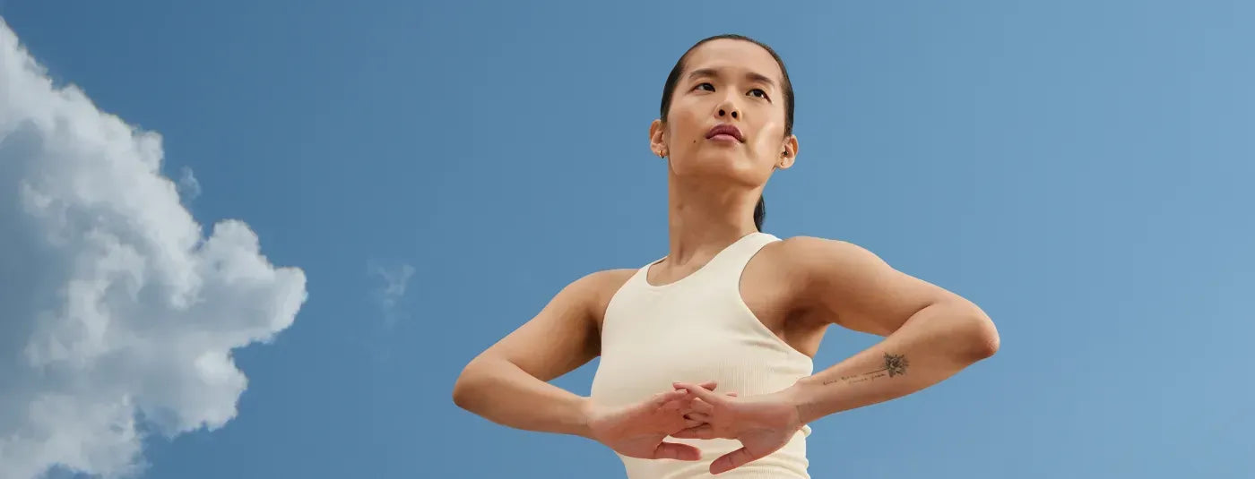 A woman stretching against a blue sky with a large cloud.