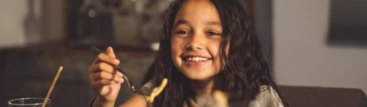 Small girl smiling and holding a fork towards her mouth.