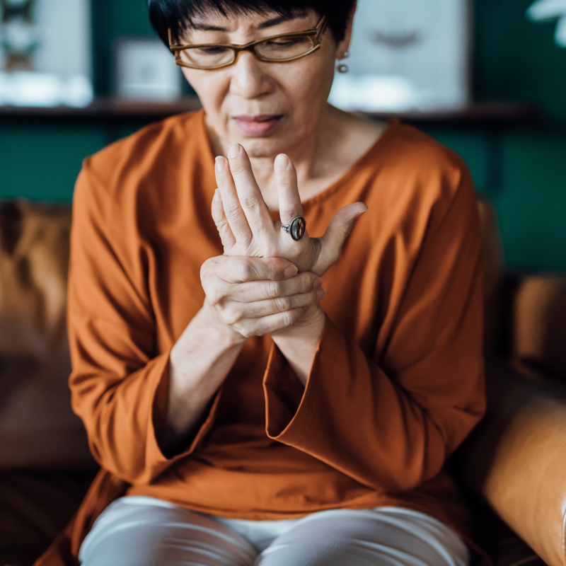 Woman in orange shirt holding her hand in discomfort