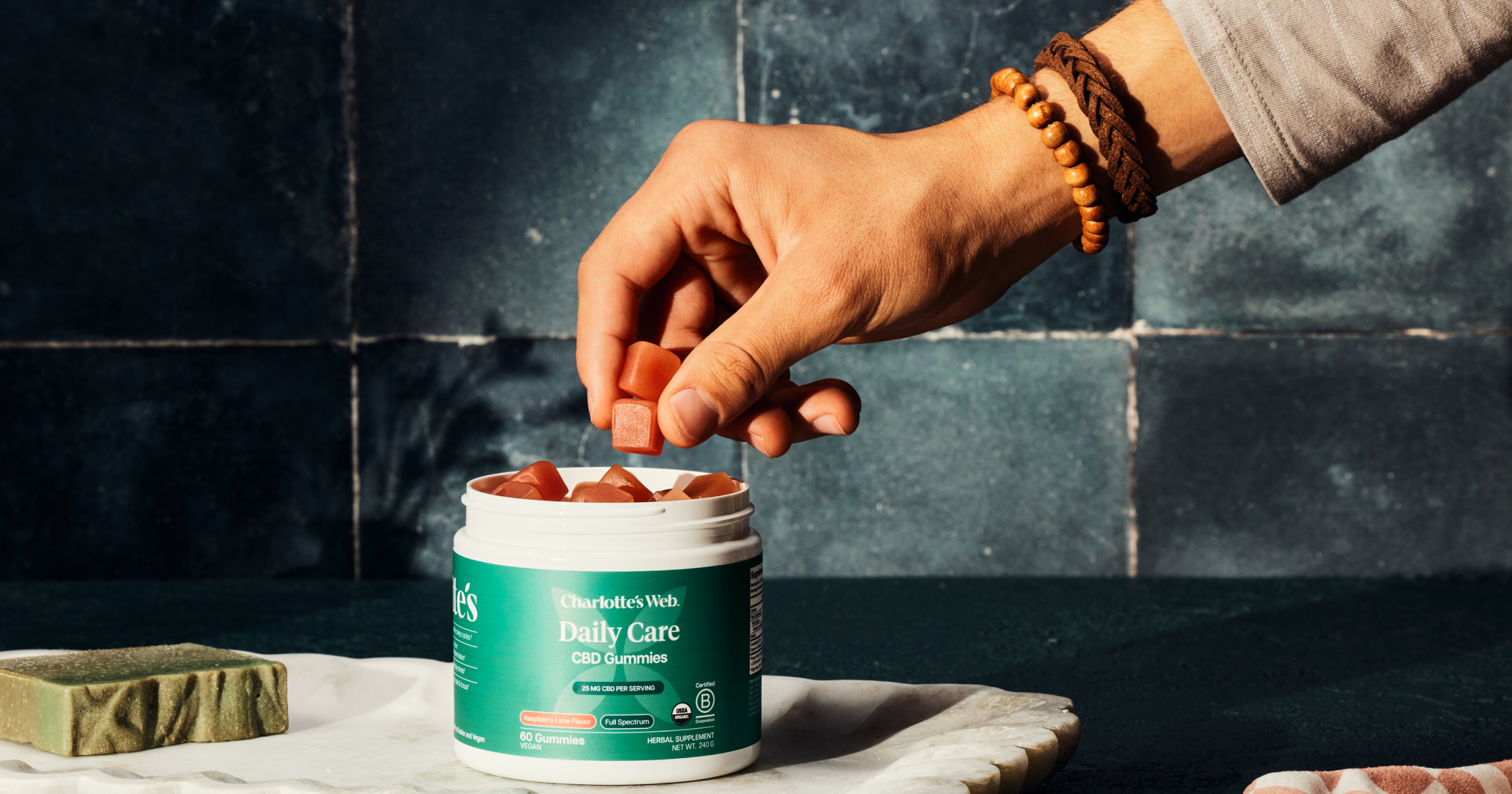 Person holding a container of Daily Clean CBD Gummies with a dark tiled background