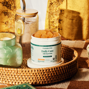 Product Image for Jar of Charlotte&#39;s Web Daily Care CBD Gummies on a woven tray with a candle and lemon water in the background.