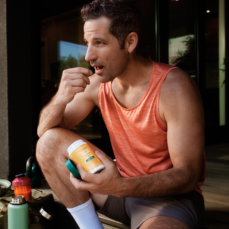 Man in an orange tank top sitting outdoors holding a energy support bottle.