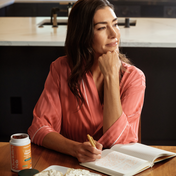 Product Image for Woman writing in notebook in kitchen with focus support supplements nearby