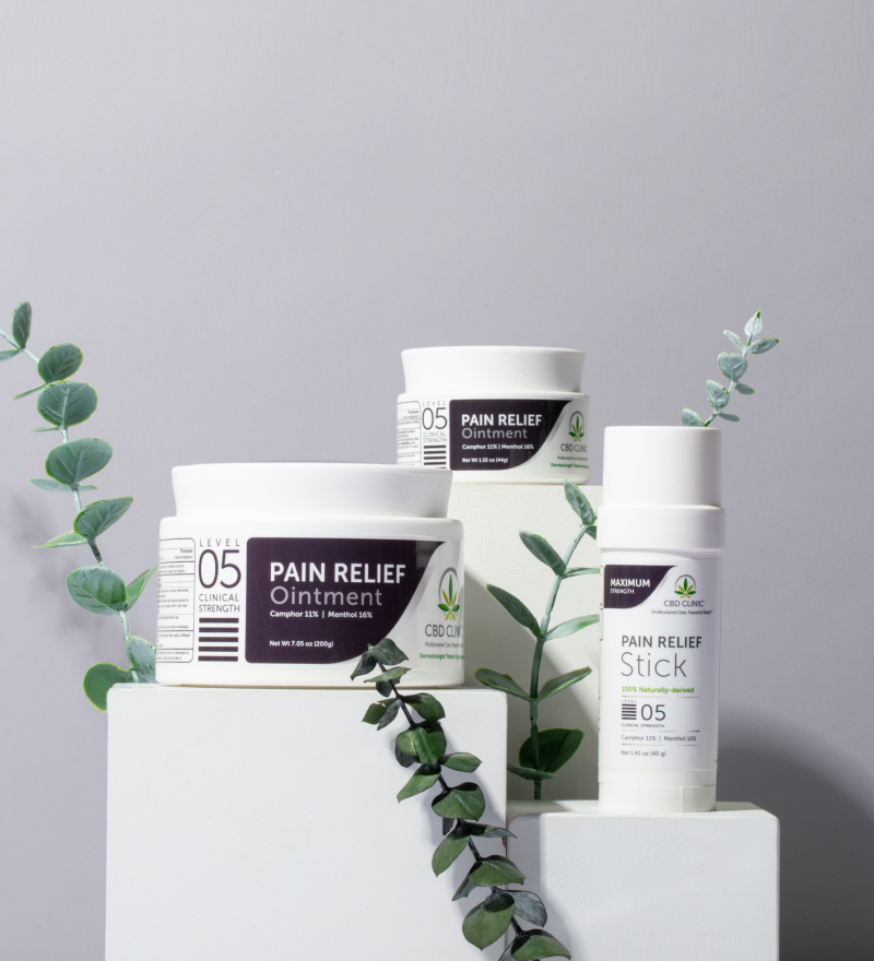 Pain relief products including ointment and stick on a gray background with green leaves.