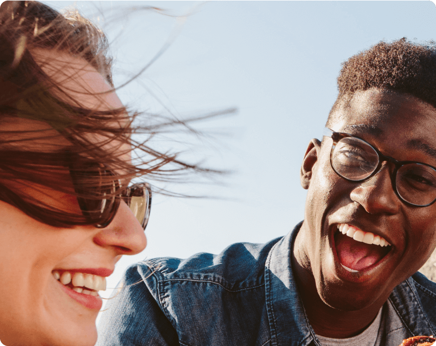 Two people laughing outdoors with a clear blue sky.