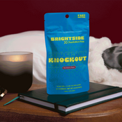 Product Image for Blue package of Brightside Charlotte&#39;s Web Knockout Blackberry gummies on a wooden surface with a candle and notebook.