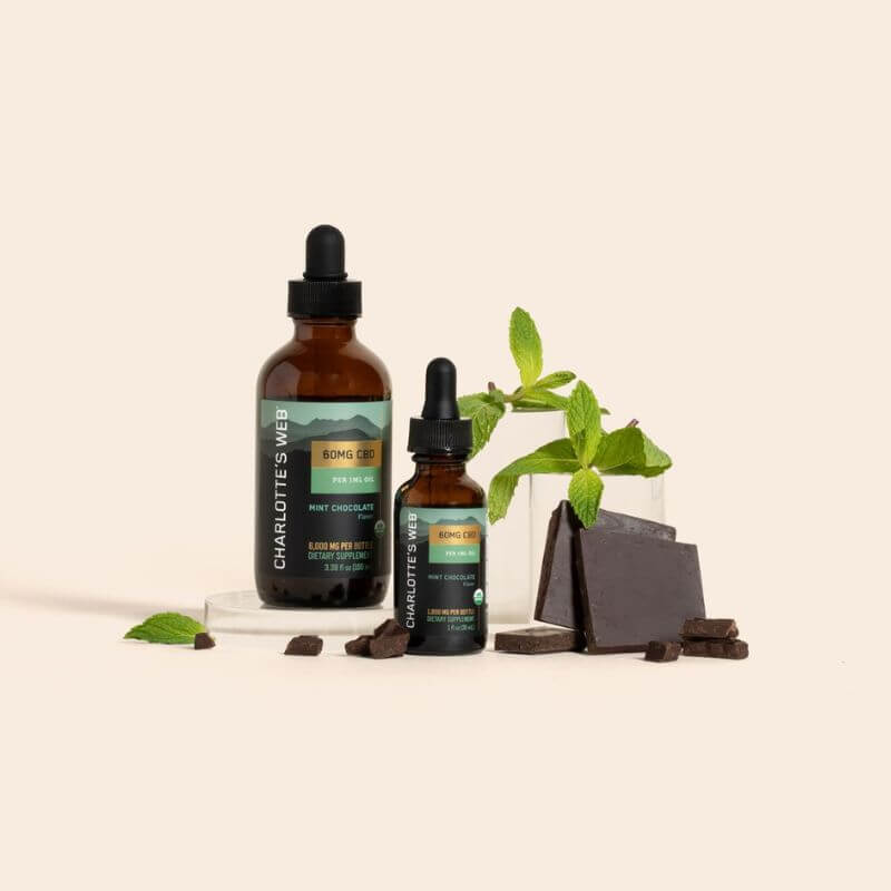 Two bottles of Charlotte's Web CBD products on a beige background with chocolate and mint leaves.