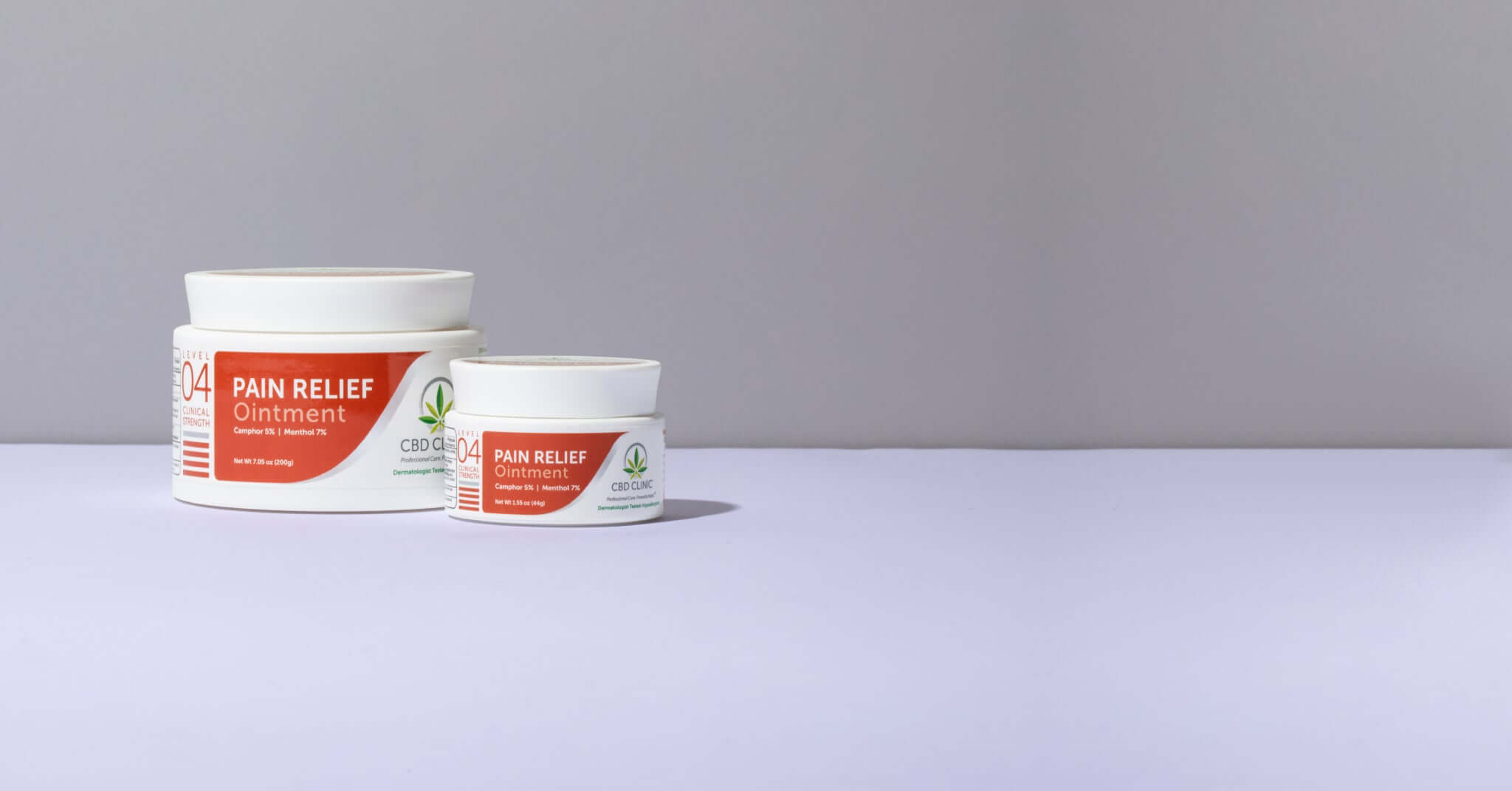 Two jars of pain relief ointment on a gray surface with a gray background